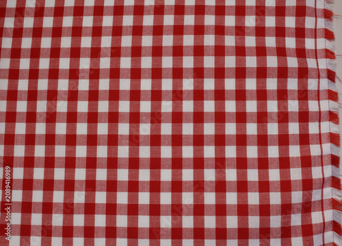 Texture of classic red plaid cotton cloth with fringed edge. Close up of red and white gingham fabric background.	