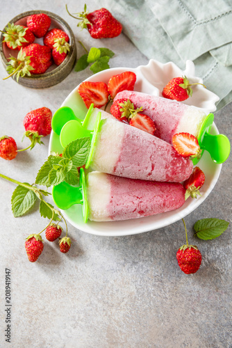 Homemade strawberry ice cream on a stick made from fresh strawberries on a textured grey stone surface. Tasty summer dessert ready to eat. Copy space.