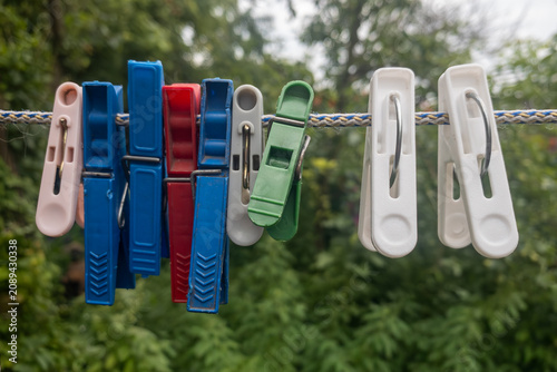 Tableau sur toile Many colorful clothespins clamping on a clothesline ready for laundry day in the fresh air with green bushes