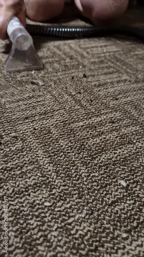 A person hand uses a clear vacuum attachment to suck up dirt and lint from a textured brown carpet. Concept of deep home cleaning, hygiene maintenance, and daily household chores.