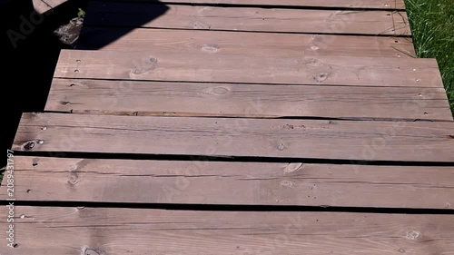 Weathered brown wooden planks of an outdoor walkway are shown in a close-up perspective under bright natural light. Concept of summer vacation, rustic design, and outdoor living space.