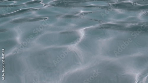 Bright sunlight creates dancing caustic patterns on the gently rippling surface of clear blue water. Concept of summer vacation, refreshing relaxation, pure environment, and peaceful travel.