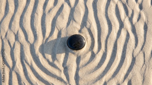 Smooth black zen stone resting perfectly in the center of patterned ripples on white sand surface