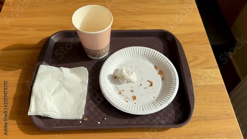 Paper plate and cup on tray close-up brown cafeteria tray with crumpled napkin, crumbs on plate, disposable cup, wooden table, warm