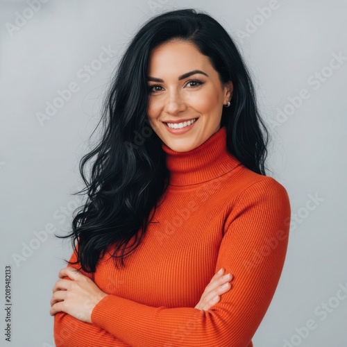Professional headshot of a smiling woman with long dark hair wearing an orange turtleneck sweater against a neutral background