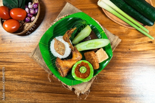 Fotografie Authentic Indonesian Cuisine: A vibrant plate of traditional Indonesian fare featuring crispy fried chicken, rice, cucumber slices, tofu, and a flavorful sambal, presented on a banana leaf
