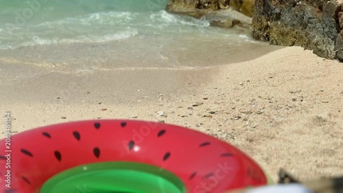 Colorful watermelon-shaped inflatable ring  on a sunny sandy beach near waves of crystal-clear turquoise water