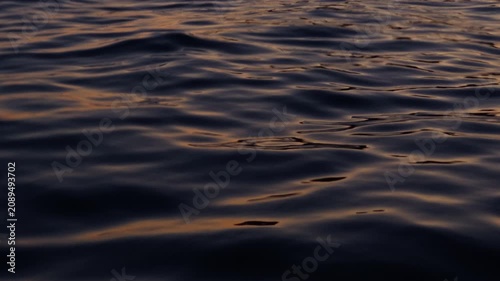 Dark ocean surface shimmering with warm golden reflections of the setting sun, waves and glowing evening light