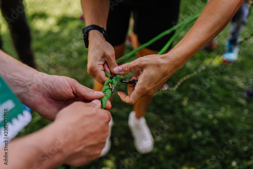 Two hands tying a green climbing rope together outdoors on grass, demonstrating teamwork and collaboration in a natural setting during a group activity