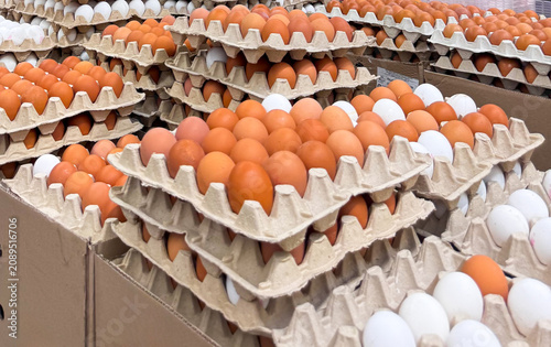 Large stack of open cardboard egg cartons filled with fresh brown and white chicken eggs arranged on boxes at a wholesale warehouse, local farmers market, or grocery store supply area.