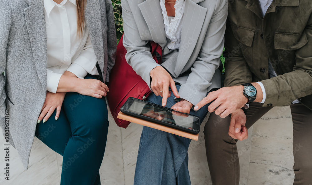 Fototapeta premium Three colleagues review content on a tablet while seated together. Casual business meeting shows collaboration and discussion over a touchscreen device.