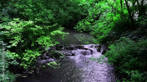 Scenic waterfall flowing through a lush green forest surrounded by rocks and vibrant vegetation. Peaceful natural landscape with fresh water, ideal for travel, nature, and environmental themes.