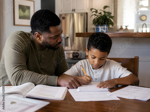 Parent Helping Child With Homework At Kitchen Table In Authentic Everyday Family Learning Environment