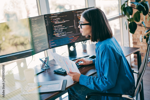 Fotografie Female programmer at a sunny loft office coding on multiple monitors while revie