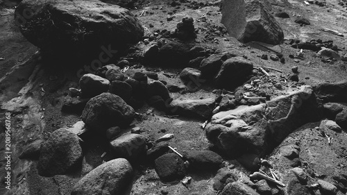 Fotografie Monochrome rocky riverbed background with large boulders, gritty sand, scattered pebbles, dry debris, and dramatic natural shadows