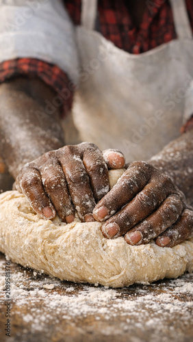 A person's hands working the dough with wheat flour, indicative of traditional and authentic baking techniques. The scene takes place in a kitchen environment.