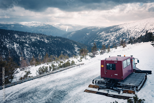 Fotografie Red snowcat tracked vehicle driving on a snowy mountain road in winter