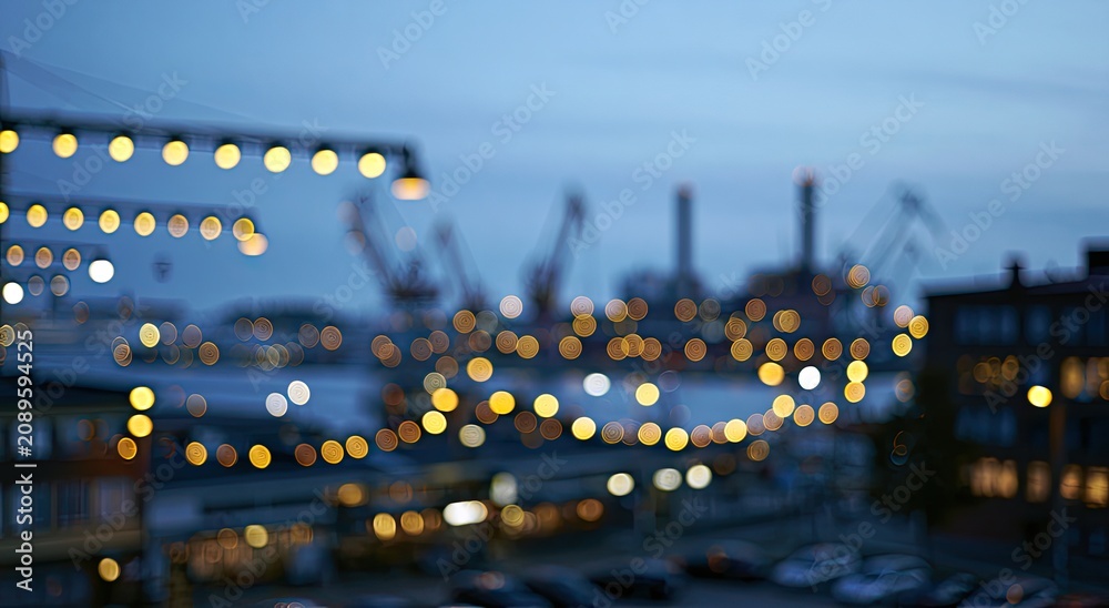 Fototapeta premium Blurry evening lights illuminate a waterfront with industrial structures and parked cars