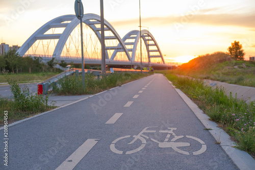 Bicycle path leads to a curved arch bridge at sunset, an outdoor urban landscape with a bike symbol on the pavement