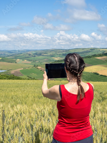 Woman Using Tablet to Photograph Scenic Wheat Field and Rural Landscape