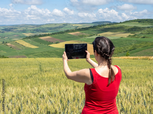 Woman Using Tablet to Photograph Scenic Wheat Field and Rural Landscape