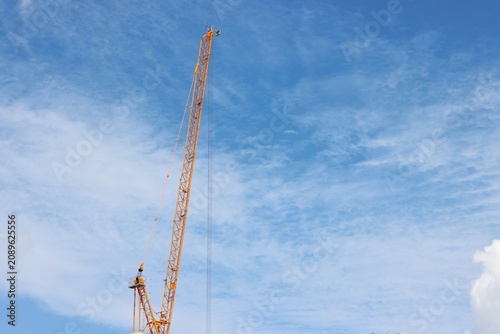 Yellow crane boom, clouds blue sky background