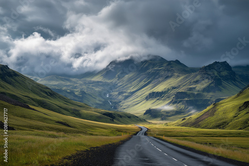 Journey Through Majestic Peaks: An empty asphalt road winds through a dramatic, verdant valley under a sky filled with moody clouds, leading towards distant, majestic mountains.