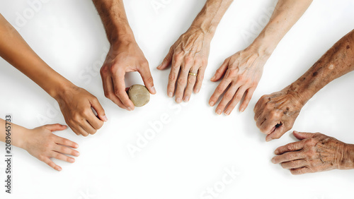 Diverse group of human hands of different ages and skin tones reaching towards a small round in the center on a white background