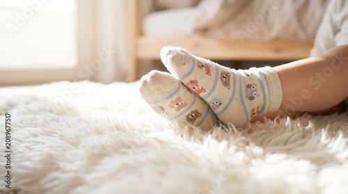 Cozy feet wearing cute animal-patterned socks resting on a soft, fluffy white rug near a sunlit window.