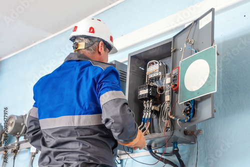 Foto Electrician in a safety helmet working on a control panel with various electrical components