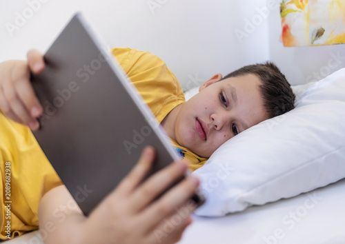 Relax, smile and kid with tablet in bedroom for game, streaming show or learning online in home. Caucasian boy, bed or happy with digital technology for movie app, cartoon or reading ebook on weekend.