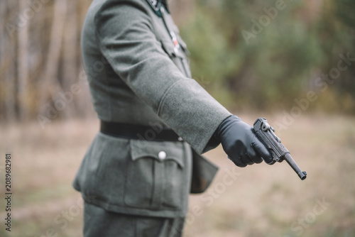 Obraz na plátně Close-up of a German officer aiming a pistol during a World War II historical reenactment