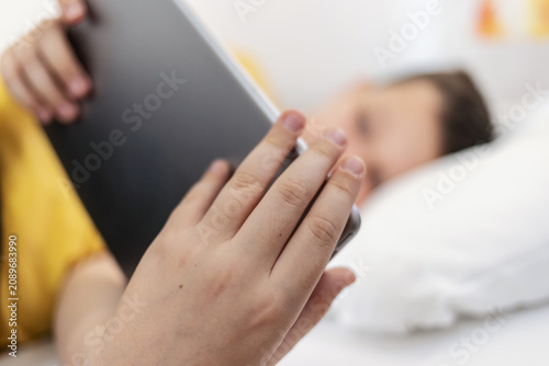 Young boy laying in bed and watching video clips on tablet. Boy lying on bed with digital tablet.