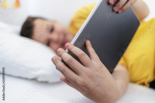 Young boy enjoys screen time in his bed, using a tablet computer to explore the digital world. Child using gadget, education and development.