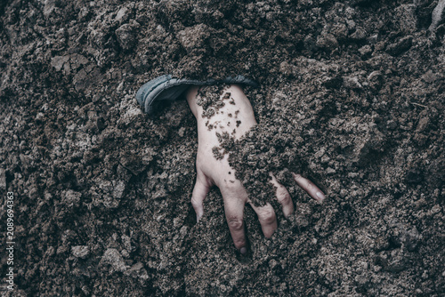 The concept of investigating war crimes. Buried human hand reaching out from dark clumpy soil. Symbol of mass grave, genocide, war crimes, and tragic historical memory.