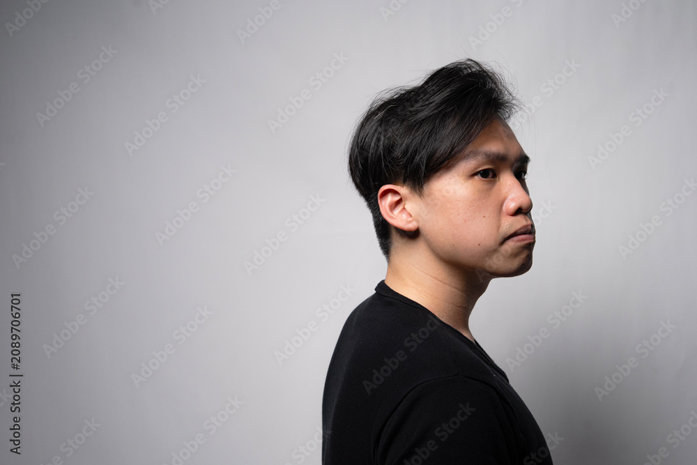Fototapeta premium Profile portrait of a thoughtful young Asian man in a black shirt looking away against a light grey background with copy space