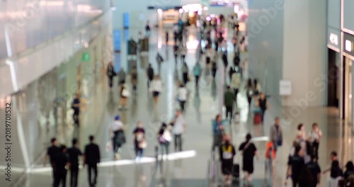 Real-time elevated view of moderately busy airport terminal corridor with intentionally defocused passengers walking past duty-free stores, anonymized motion captures essence of modern travel
