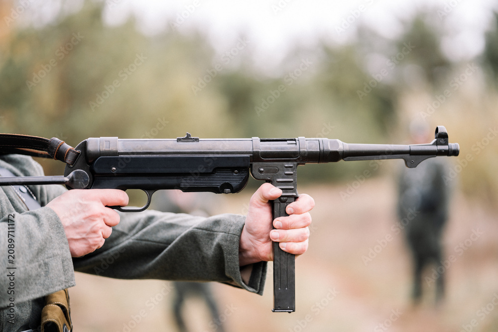 Obraz premium Close-up of hands firing an MP-40 submachine gun during a historical reenactment. 