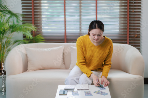 Asian woman managing personal finances at home, counting cash money and calculating expenses on a calculator, planning savings, budgeting, and debt repayment