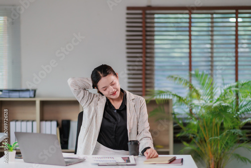Картината върху платно Young Asian businesswoman sitting at her office desk, feeling tired and stressed