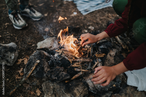 Fotografie Hands arranging kindling as a small campfire burns on a rocky ground