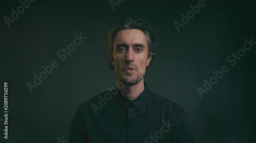 Serious adult man portrait in black shirt facing camera with neutral expression, soft diffuse lighting, shallow depth of field, dark minimal studio background