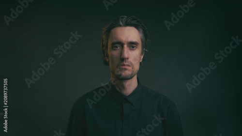 Young man nodding yes, close up portrait with tousled hair in black shirt, soft dramatic lighting on dark studio background