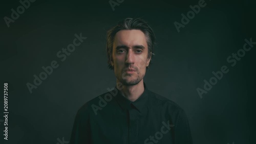 Young adult man portrait with medium-length dark hair in black button-up shirt, low-key lighting, shallow depth of field, dark blurred background