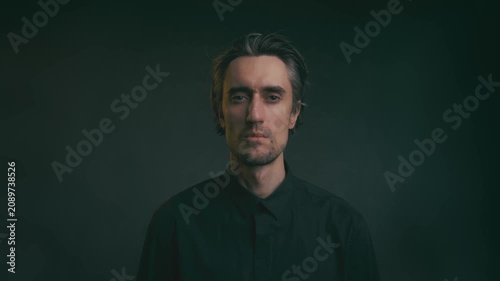 Young man making no gesture, shaking head in studio portrait, medium-length tousled hair, black button-up shirt, dark background, soft lighting