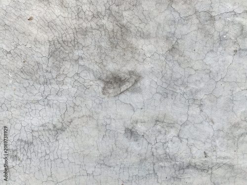 A close up view of a weathered concrete wall surface featuring intricate cracks and a rough gray texture suitable for industrial design backgrounds.