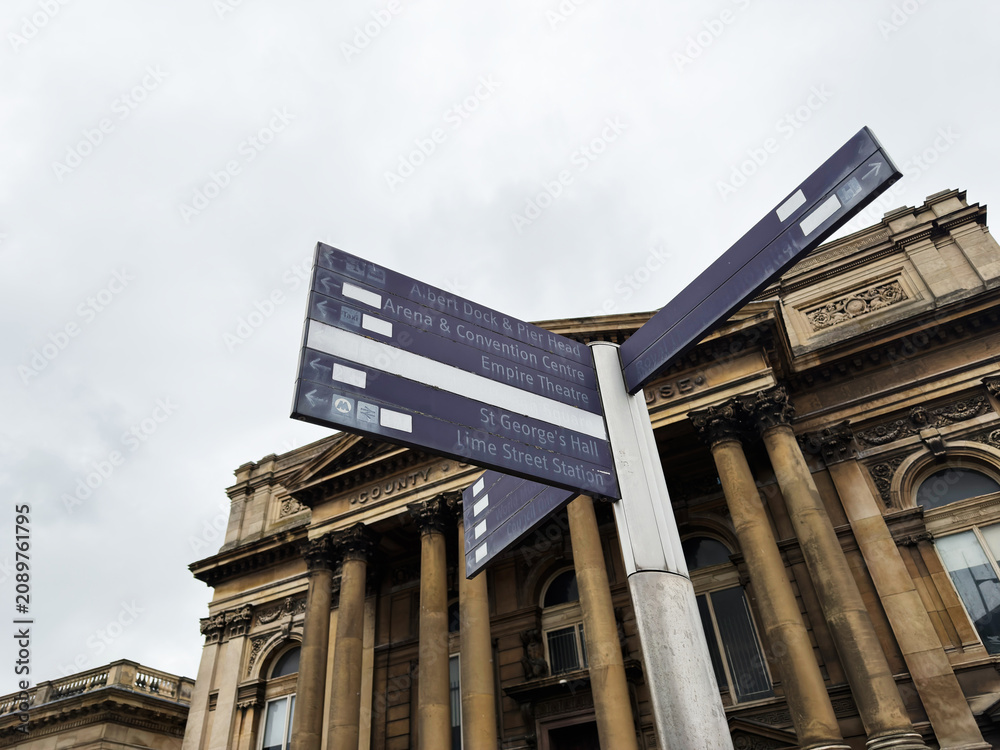Obraz premium Historic directional signpost pointing to attractions in front of a classical museum facade in Liverpool, UK on an overcast day