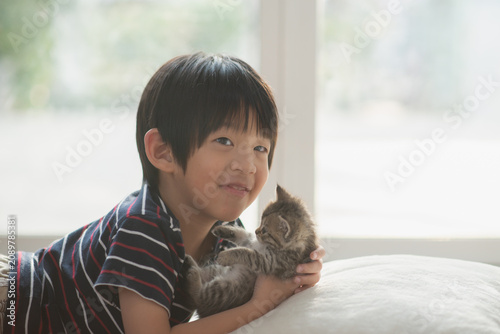 A happy Asian boy smiling and holding a cute tabby kitten, relaxing at home, friendship and love concept.