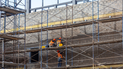 Builders, standing on metal scaffolding, install a reinforcing mesh for applying plaster. The work at height is carried out by builders. Cladding works during the construction of the building.