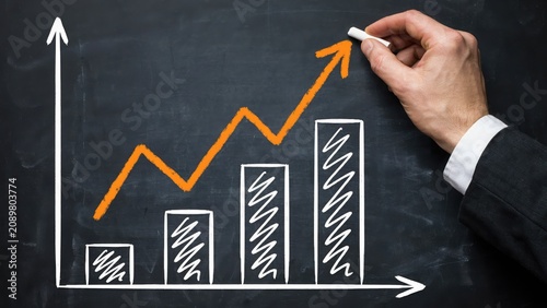 Business person hand drawing a growing bar chart and arrow on a black chalkboard